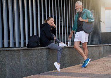 Aktif orta yaşlı sporcular, spor giysili kadın ve erkek dışarıda antreman için beklerken sohbet ediyorlar.