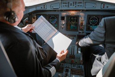 Uçak pilotu kokpitteki uçuş öncesi belgeleri inceliyor.