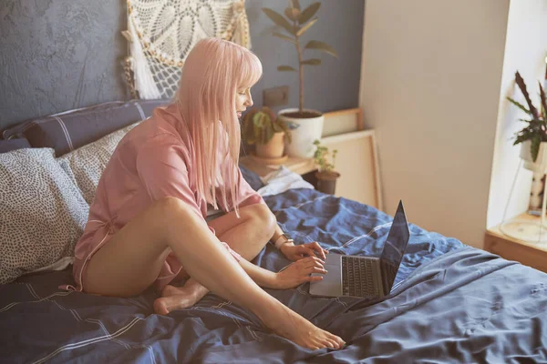 Positieve vrouw met types op hedendaagse laptop toetsenbord zitten op bed — Stockfoto