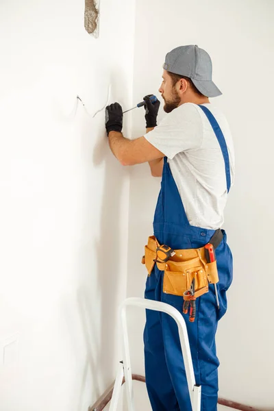 Concentrated electrician, handyman using screwdriver while working on installing socket on wall at home — Fotografia de Stock