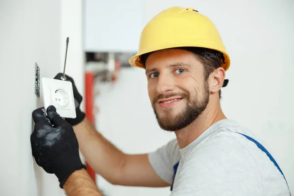 Confident professional electrician in uniform using screwdriver while replacing a socket in apartment after renovation work — Stock Photo, Image