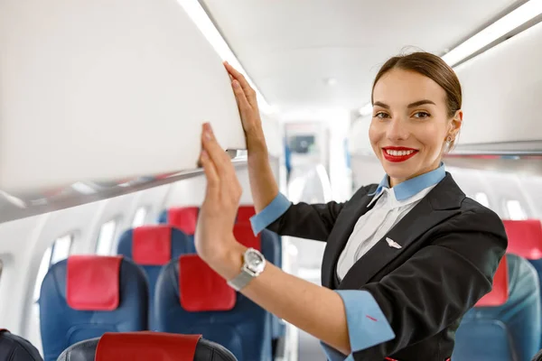 Veselá letuška stojící nad hlavou zavazadlového prostoru v letadle — Stock fotografie