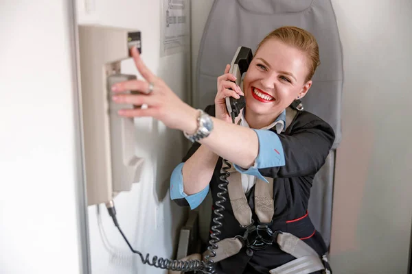 Joyful flight attendant talking on telephone in airplane cabin — Stockfoto