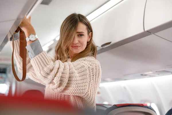 Mujer poniendo la bolsa en la papelera de equipaje en el avión — Foto de Stock