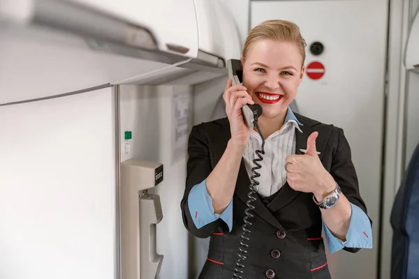Radostná letuška mluví po telefonu a dává palce nahoru — Stock fotografie