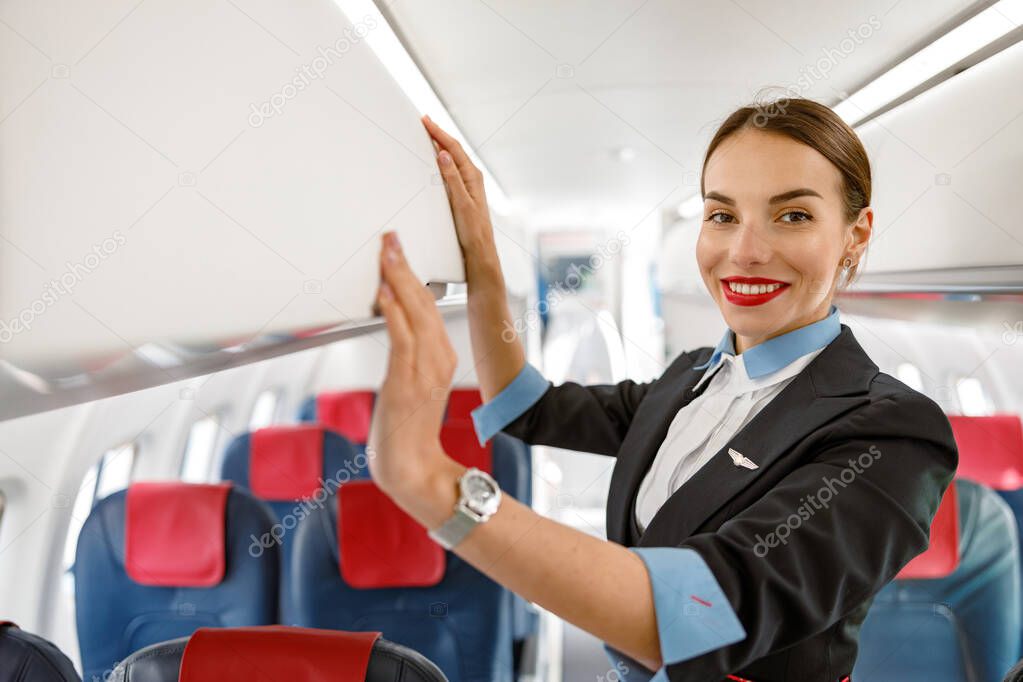 Cheerful stewardess standing by overhead luggage bin in aircraft