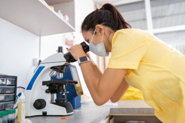 Kadın araştırmacı laboratuarda mikroskopla çalışıyor.