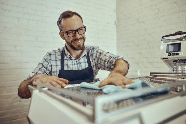 Kafede kahve makinesini temizleyen neşeli erkek barmen.