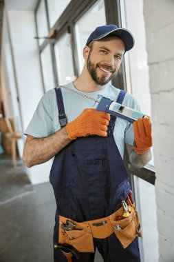 Neşeli adam pencereyi silikon yapıştırıcı tabancayla onarıyor.