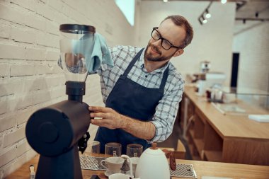 Kafede kahve makinesini temizleyen gülümseyen erkek barmen.
