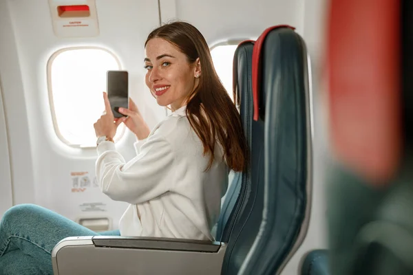 Radosna kobieta robiąca zdjęcia smartfonem w samolocie — Zdjęcie stockowe