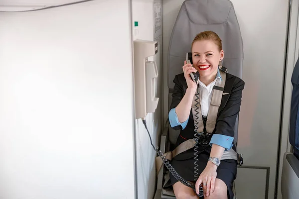 Cheerful stewardess talking on telephone in airplane cabin — Stockfoto