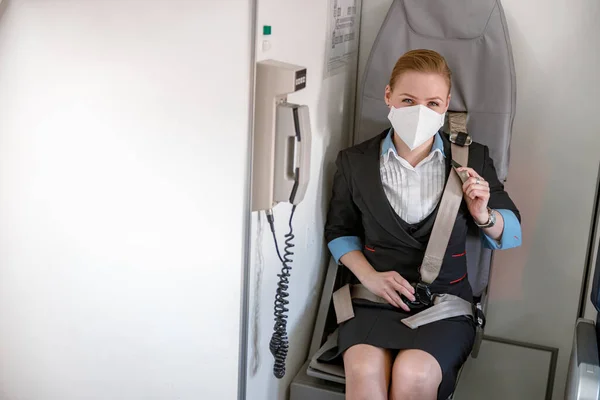 Stewardess in medical mask fastening seatbelt in aircraft — Stockfoto