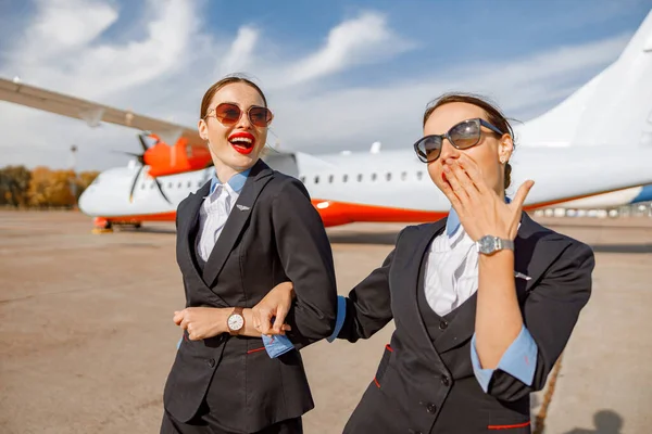 Joyful flight attendants walking arm in arm at airport — Stock fotografie