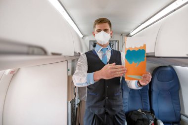 Male flight attendant in medical mask holding instruction booklet