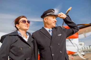Neşeli uçak pilotu ve hostesi havaalanında dikiliyor.