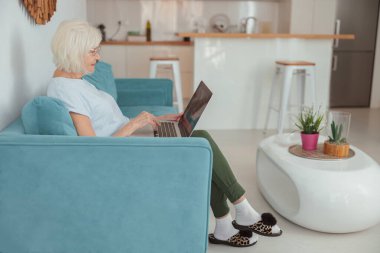 Kafkasyalı emekli kadın içeride dizüstü bilgisayarda çalışıyor.