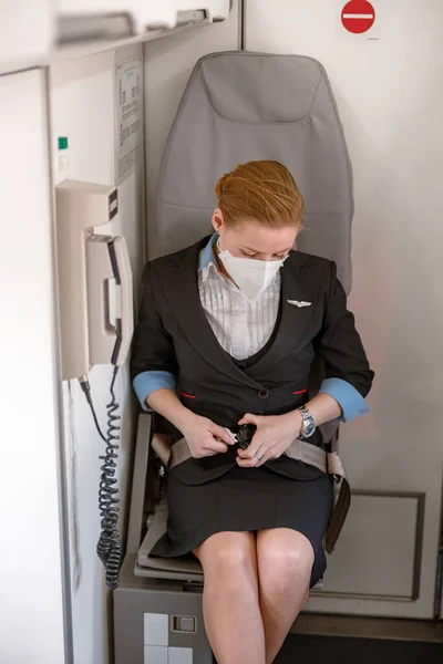 Flygvärdinna i säkerhetsbälte för medicinsk mask i flygplan — Stockfoto