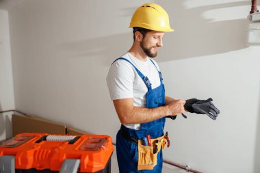 Üniformalı profesyonel elektrikçi ve şapka takan koruyucu eldiven takan kapalı alanda duran.