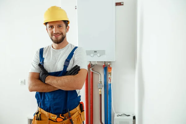 Técnico sonriente que mantiene el sistema de calefacción de la casa mirando a la cámara mientras está de pie con los brazos cruzados —  Fotos de Stock