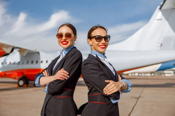 Veselé letušky stojící zády k sobě na letišti — Stock fotografie