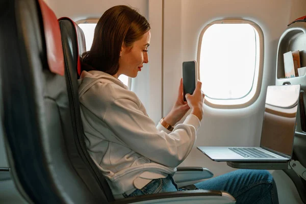 Jonge vrouw maakt foto met smartphone in vliegtuig — Stockfoto