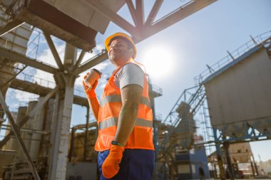 Büyük bir inşaat fabrikasının önünde deneyimli bir işçi duruyor.