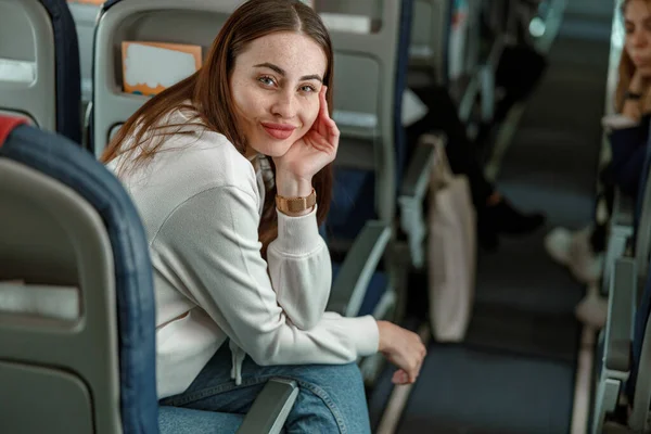Mujer joven sonriente sentada en un avión de pasajeros — Foto de Stock