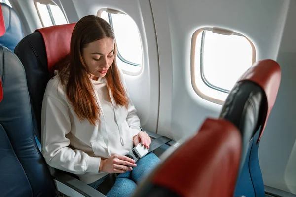 Joven mujer abrochándose el cinturón de seguridad en avión de pasajeros — Foto de Stock