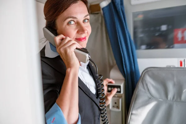 Kvinnlig flygvärdinna pratar i telefon i flygplan — Stockfoto