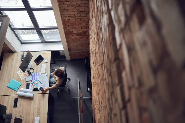 Вид сверху женщины-дизайнера, читающей синий принт, подбирающей цветовые образцы при работе над новым проектом дизайна интерьера в современном офисе — стоковое фото