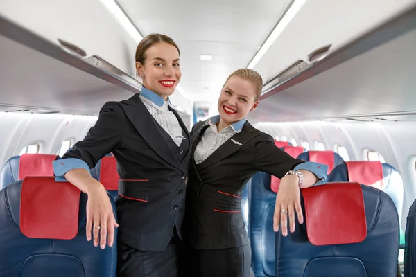 Alegre azafatas mujeres de pie en cabina de avión de pasajeros —  Fotos de Stock