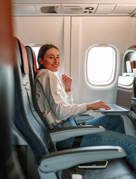 Радісна молода жінка використовує блокнот у літаку — стокове фото