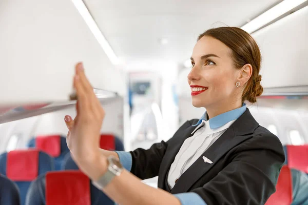 Usmívající se žena letuška zavírající nad hlavou zavazadlový prostor v letadle — Stock fotografie