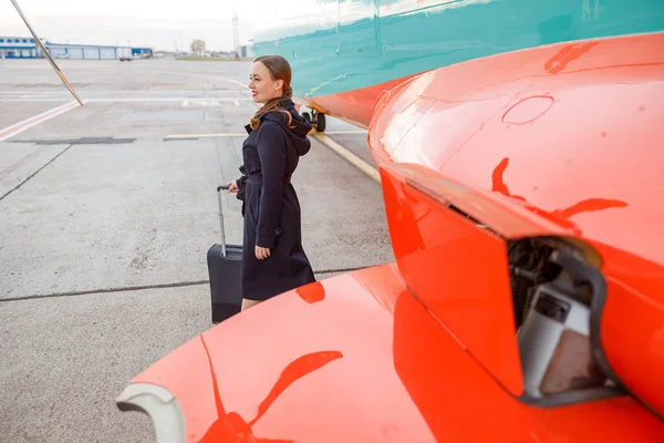Veselá žena s cestovní taškou stojící u letadla na letišti — Stock fotografie