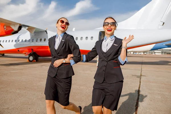 Usmívající se ženy letušky chůze ruku v ruce na letišti — Stock fotografie