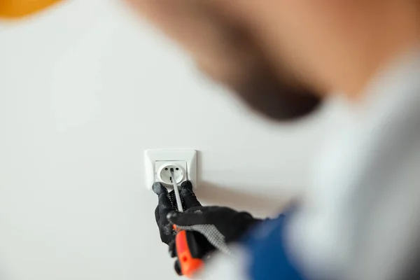 Menutup tangan pekerja laki-laki, tukang listrik profesional dalam sarung tangan pelindung menggunakan obeng saat memasang soket listrik baru di sebuah ruangan — Stok Foto
