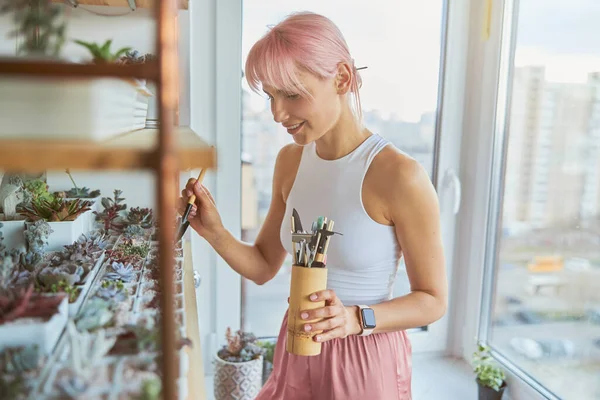 Wanita berambut merah muda cantik merawat tanaman rumah di balkon di rumah — Stok Foto