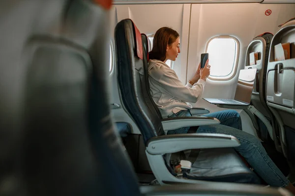 Mujer joven tomando fotos con teléfono celular en avión — Foto de Stock