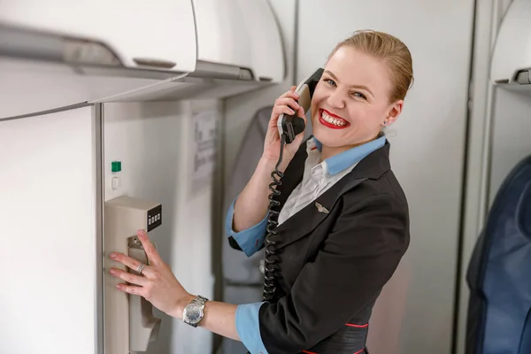 Asistente de vuelo alegre hablando por teléfono en cabina de avión — Foto de Stock