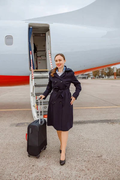 Veselá žena s cestovní taškou stojící venku na letišti — Stock fotografie