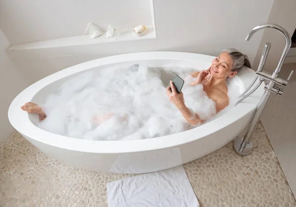 Senhora relaxante no banho e falando ao telefone — Fotografia de Stock