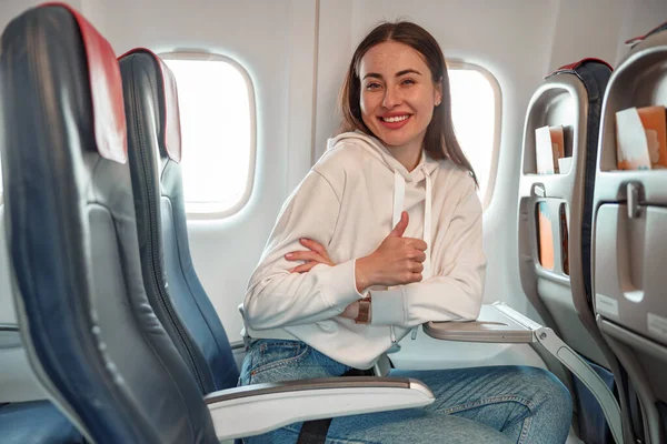 Radostná mladá žena dělá palce nahoru gesto v letadle — Stock fotografie