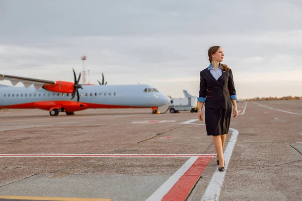 Žena letuška kráčí po letišti pod bílou oblohou — Stock fotografie