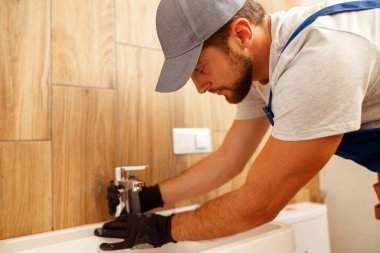 Ciddi tesisatçı, üniformalı erkek işçi musluk ya da banyo musluğu takıyor.