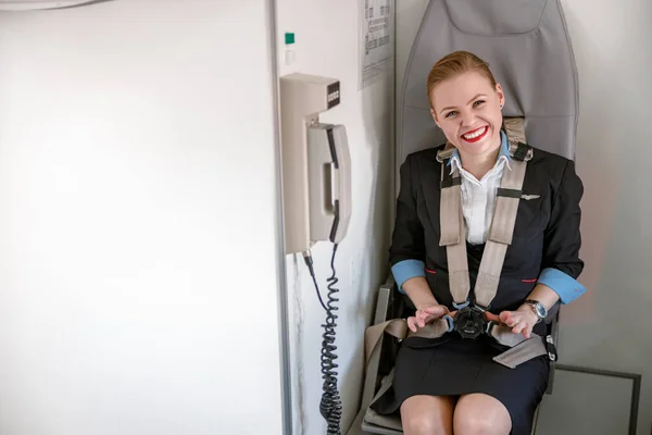 Glada kvinnliga flygvärdinna sittande i stol i flygplan — Stockfoto