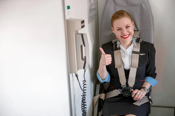 Alegre azafata haciendo pulgares hacia arriba gesto en cabina de avión —  Fotos de Stock