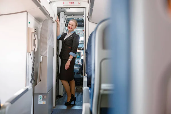 Glada flygvärdinna står vid utgången dörren i flygplan — Stockfoto