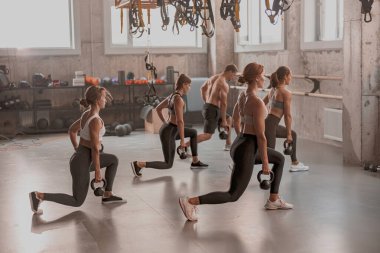 Spor salonunda kettlebell egzersizi yapan bir grup insan.