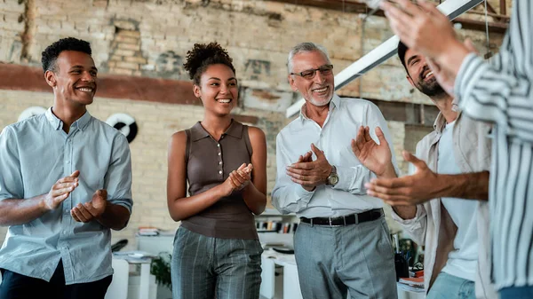 Equipo multicultural aplaudiendo y sonriendo mientras están de pie en la oficina creativa — Foto de Stock